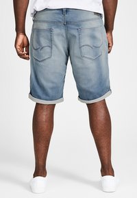 Pantalones cortos de denim con un acabado azul desgastado, puños enrollados y dos bolsillos traseros con sutiles detalles de costura. Llevados con zapatillas blancas.