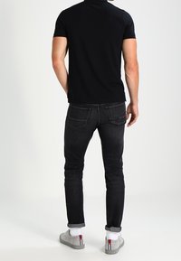 Svart kortärmad skjorta, slim-fit mörka jeans, grå sneakers med röda accenter, avklippta nederkant, synliga bakfickor.