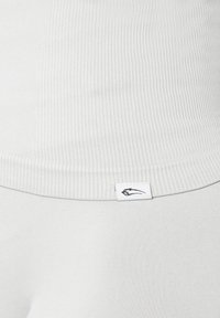 Lys grå ribbet tanktop med et tætsiddende design, der har et lille sort logo mærke ved nederkanten. Blød tekstur og sømløs finish.