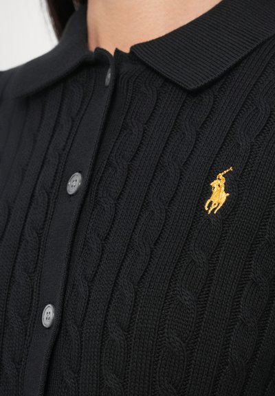 Čierny pletený polokošeľový sveter so vzorom káblového pletenia, vybavený žribovaným golierom, sivými gombíkmi a zlatým vyšívaným logom. Detailný záber na textúru a detaily látky.