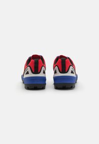 Rote und schwarze Sportschuhe mit einer blauen Sohle, ausgestattet mit verstärktem Absatz und strukturiertem Außensohlenprofil für besseren Halt, entworfen für Leistung und Langlebigkeit.