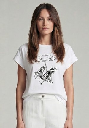 Frau mit langen braunen Haaren trägt ein weißes T-Shirt mit einer schwarz-weißen Grafik von Strandstühlen und Sonnenschirm, kombiniert mit weißen Hosen.