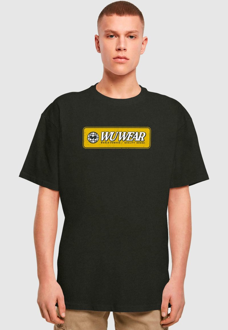 Melnas kokvilnas T-krekls ar dzeltenu taisnstūra grafiku, kurā rakstīts "WU WEAR" un ir globusa logo. Īsas piedurknes un brīvs piegriezums.