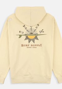 Sweatshirt à capuche crème avec un imprimé graphique représentant un soleil et des éléments de surf, étiqueté "SURF SUPPLY SINCE 1985" en texte marron.