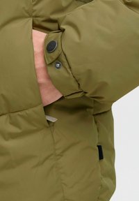 Manga de chaqueta acolchada verde oliva con cierre de botón a presión y bolsillo lateral. Textura suave con costuras visibles y puño doblado.