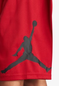Pantalones cortos de baloncesto rojos, hechos de un tejido de malla texturizada, que presentan un gran logo de Jumpman negro en el lado izquierdo.