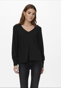 Blusa preta de mangas longas com decote em V, apresentando um corte descontraído e detalhes em botões nas mangas. Feita de um tecido suave e liso.