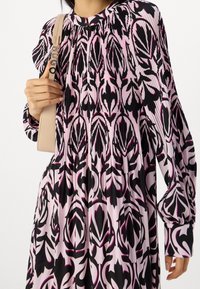 Volná šaty s plisovanou texturou, které mají černý a růžový květinový vzor, kulatý výstřih a dlouhé nabírané rukávy. Připojený béžový pásek.