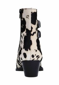 Bottines en cuir de vachette noir et blanc avec une surface texturée, petit talon carré et boutons décoratifs sur le côté.