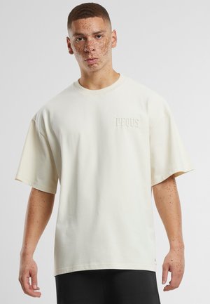 Krämfärgad t-shirt med korta ärmar, tillverkad av bomull, med en loose fit, rund hals och präglad logotyp på vänster bröst.