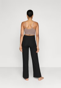 Brun ribbet crop top med tynde stropper parret med højtaljede sorte bukser med vidde, begge tætsiddende og glatte i teksturen.