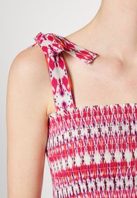 Top corto con fruncidos que presenta patrones multicolores en rosa y blanco, con lazos ajustables en los tirantes y un acabado de tela texturizada.