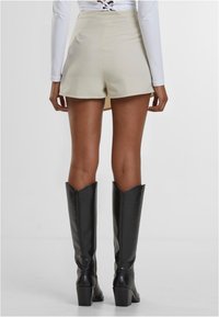 Beige high-waisted shorts dengan tekstur halus, dipasangkan dengan sepatu bot kulit hitam setinggi lutut yang memiliki hak blok dan ujung runcing.