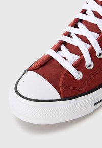 Shoe de lona vermelha com atacadores brancos e biqueira de borracha. Sola de borracha branca com padrão de aderência texturizado, ilhós de aço para os atacadores.