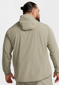 Lichtbeige jas met ritssluiting en capuchon, gemaakt van glad, lichtgewicht materiaal. Heeft een rechte snit en lange mouwen.