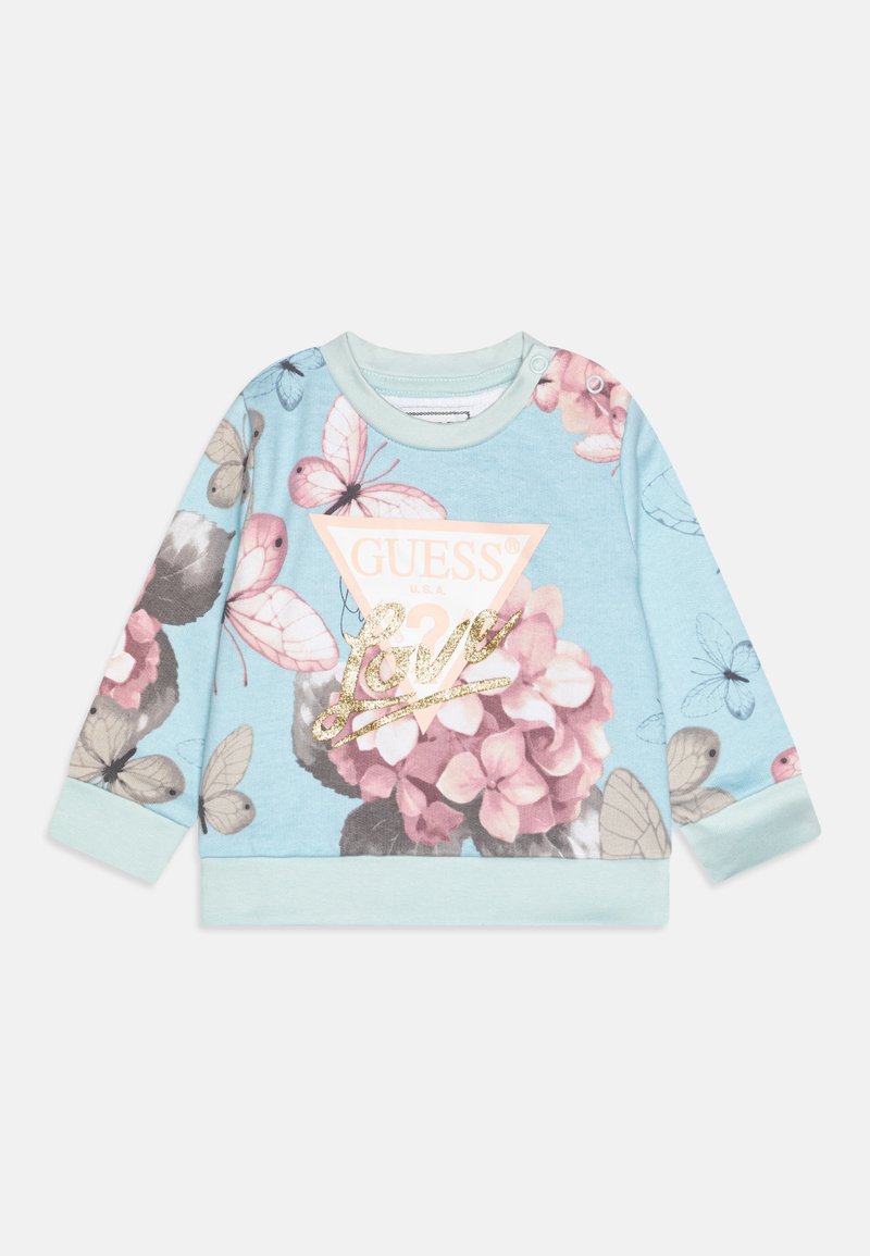 Felpa azzurra chiara con motivi floreali e farfalle, dotata di un logo triangolare rosa "GUESS" e testo dorato "Love" come accento. Materiale in cotone.