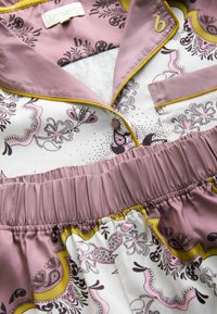 Set de pijamale din mătase în nuanțe de mauve și alb. Prezintă modele florale și paisley, cu margini galbene de-a lungul gulerului și taliei. Talie elastică.