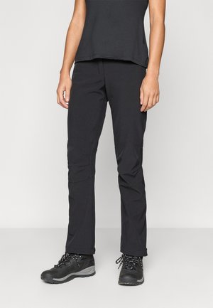 Pantalones exteriores negros con un diseño ajustado, que cuentan con parches en las rodillas y una textura suave. Llevados con botas de senderismo oscuras.