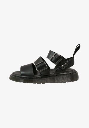 Black sandals featuring two wide straps with buckle closures, a smooth leather upper, and a thick textured sole.