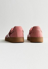 Sneaker in suede rosa con strisce bianche; tacco rotondo, suola in gomma marrone testurizzata. La vista posteriore mette in evidenza il design e le cuciture decorative.
