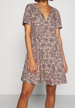Robe florale avec un décolleté en V profond, des manches courtes et une jupe évasée. Le tissu a une finition douce et texturée, avec des motifs floraux roses et violets.