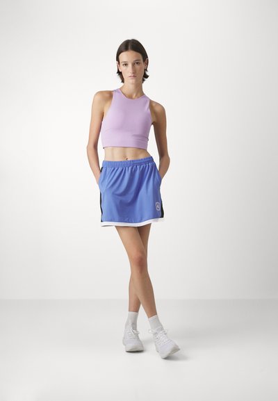En lilas topp med rund hals, parret med en blå sportskort nederdel med hvid kant og sorte sideaccenter. Hvide sneakers fuldender looket.