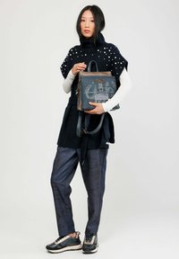 Sac à main bleu avec un motif texturé, doté d'accents marron et d'une fermeture éclair, tenu par un mannequin vêtu d'une tenue en noir et blanc.