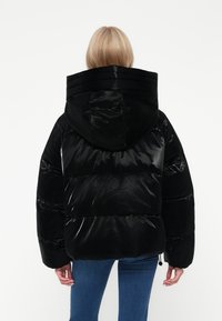 Černá péřová bunda s lesklým povrchem, oversized kapucí a horizontálním prošíváním. Zadní část má elastický lem a manžety.