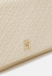Beige geprägte Handtasche mit geometrischem Muster. Sie verfügt über Beschläge in goldfarbener Ausführung mit einem Logodetail und einer glatten, matten Textur.