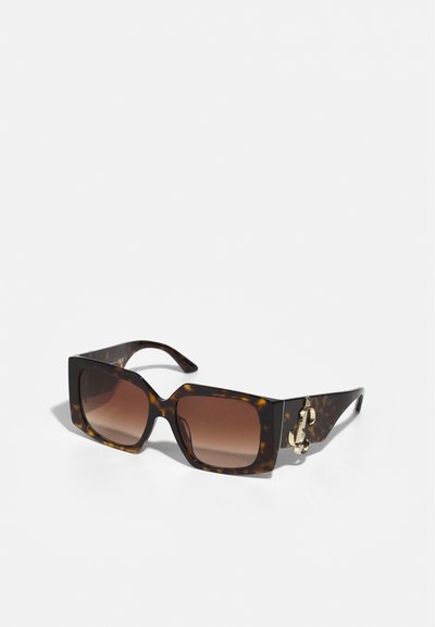 Quadratische Sonnenbrille mit einem Schildpatt-Rahmen, braunen Verlaufslinsen und einem goldenen Hardware-Akzent an der Seite. Strukturierte Oberfläche.