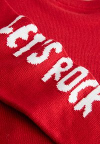 Rød strikket sweater med fed hvid tekst, der tydeligt står "LET'S ROCK" på forsiden. Glat tekstur med rund halsudskæring.