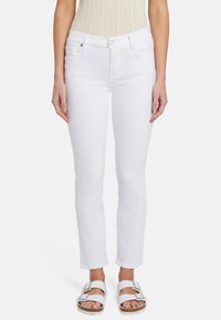 Jean en denim blanc avec une coupe slim, taille mi-haute, cinq poches et détails en métal argenté. Associé à des sandales blanches.