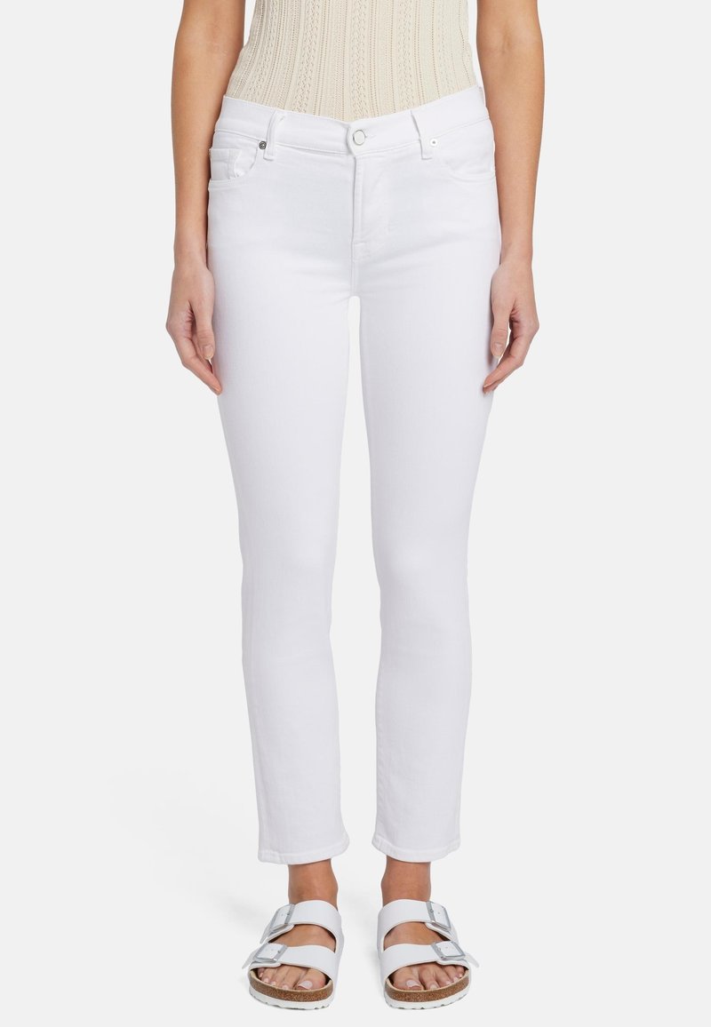 Jean en denim blanc avec une coupe slim, taille mi-haute, cinq poches et détails en métal argenté. Associé à des sandales blanches.