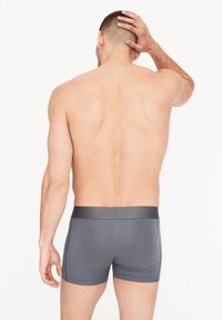 Bóxer gris para hombre hecho de material suave, con una cinturilla lisa y diseño ajustado, que presenta costuras mínimas y sin patrones visibles.
