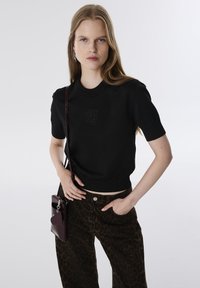 Maglione nero a maniche corte con logo "swag" in rilievo e scollatura a costine, abbinato a pantaloni larghi con stampa leopardata marrone e una borsa bordeaux.