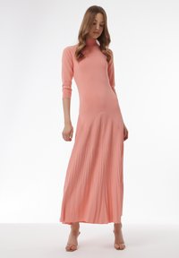 Lang, geribbeld roze jurk met een hoge halslijn, voorzien van geplooide rokdetails en driekwartmouwen. Gladde textuur en een aansluitend lijfje.