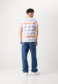 Camiseta de algodón a rayas en colores azul, naranja y blanco; combinada con pantalones vaqueros de corte holgado. Cuello redondo simple.
