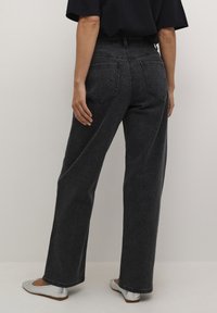 Jeans negros de tiro alto con un corte de pierna ancha, que cuentan con bolsillos traseros y un acabado sutilmente texturizado. Combinados con unas bailarinas plateadas.