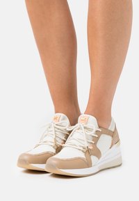 Sneaker beige e bianco con tessuto a rete e dettagli in pelle. Presenta punta rotonda, lacci e suola imbottita. Dettagli in metallo dorato.