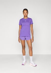 Purple athletic outfit featuring a short-sleeve top and matching shorts, made of smooth fabric. White ankle socks and light shoes with pink accents.