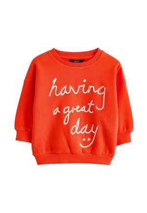 Sweat-shirt orange vif avec poignets et col côtelés, arborant un texte en cursive blanche "having a great day" et un visage souriant.