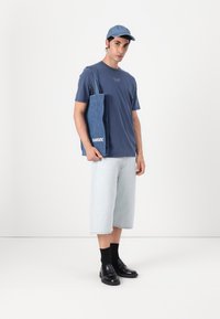 Blue t-shirt, light blue denim shorts, denim tote with "SAMSOE" logo, blue cap, black socks, and black loafers. Simple, casual outfit.
