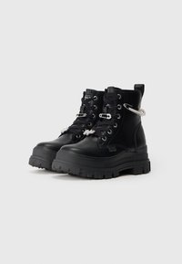 Ζευγάρι μαύρες πλατφόρμες στρατιωτικές μπότες με χοντρές σόλες, μαύρα κορδόνια και διακοσμητικές ασημένιες καστάνιες ασφαλείας προσαρτημένες μπροστά και στα πλάγια.