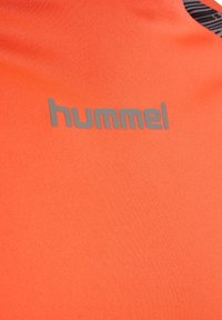 Orange Hummel träningsskjorta med en slät textur, med en grå logotyp tryckt på tyget. Designen inkluderar svarta accenter med linjer.