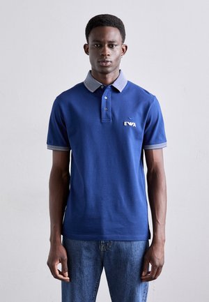 Navy blue polo shirt with a striped collar, short sleeves, and a small embroidered logo on the chest. Material appears smooth and casual.