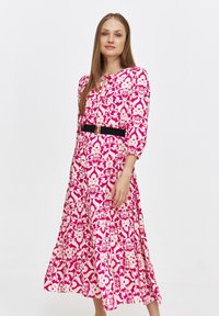 Długa różowa i biała sukienka w kwiaty z rękawami o długości trzech ćwiartek, zebranym detalem, warstwową spódnicą oraz czarnym paskiem podkreślającym talię.