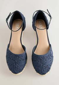 Sandales espadrilles bleu marine avec brides à la cheville, ornées d'une broderie tourbillonnante complexe et de semelles en jute tressé, vues de dessus.