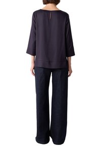 Blusa navy con maniche a tre quarti, scollatura quadrata, apertura a chiave sul retro con bottone, tessuto liscio, abbinata a pantaloni in denim scuro a gamba larga.