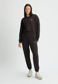 Sudadera negra y joggers a juego hechos de una tela suave, con un logo redondo en el pecho y puños y tobillos elásticos.