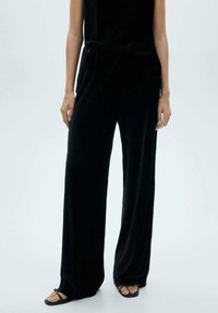 Pantaloni negri cu croială largă, din material ribbed, cu talie elastică, asortați cu sandale negre cu barete. Textură netedă cu un design fluid.